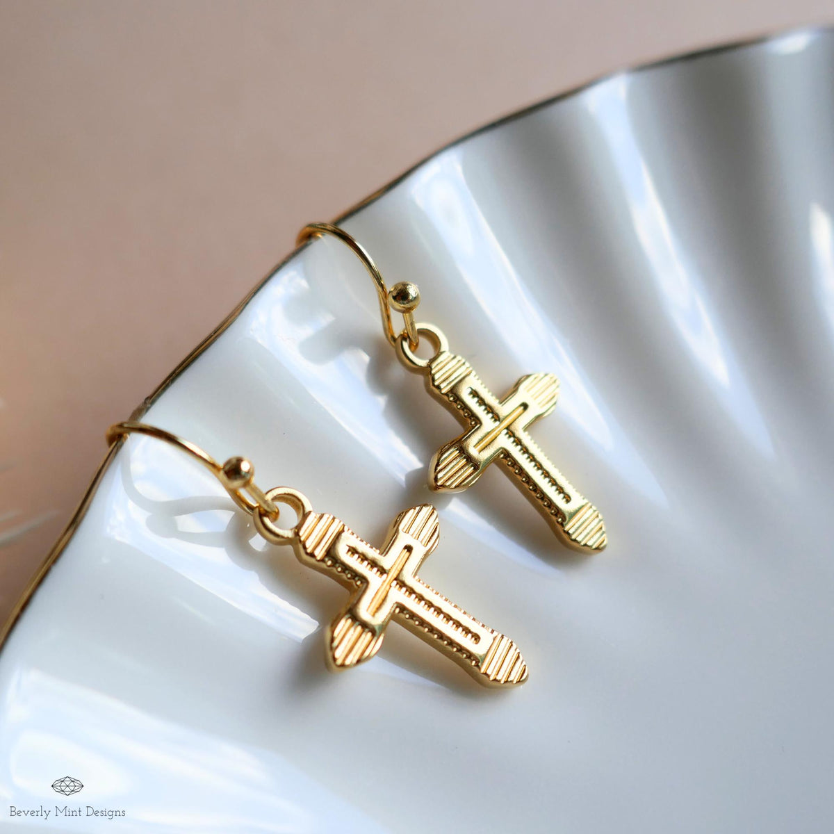 A pair of gold cross earrings with intricate designs, resting on a white surface.