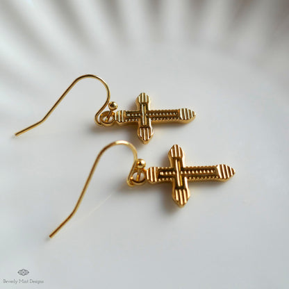 A pair of gold-colored earrings with a cross design, resting on a white surface.