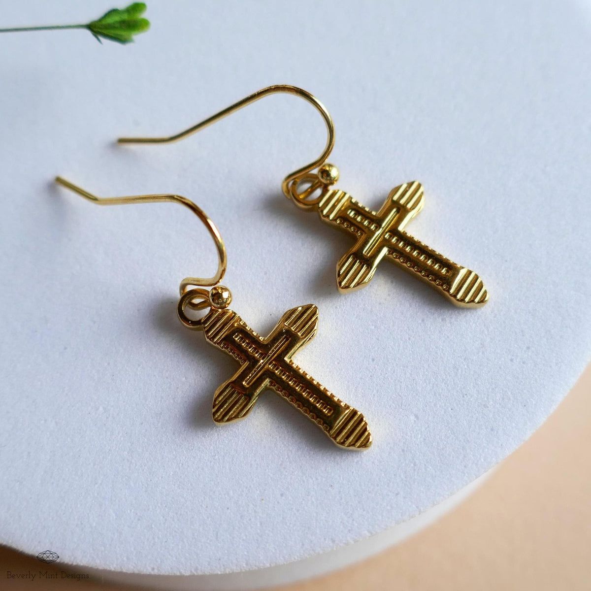 A pair of gold cross earrings with a textured design, resting on a white surface.
