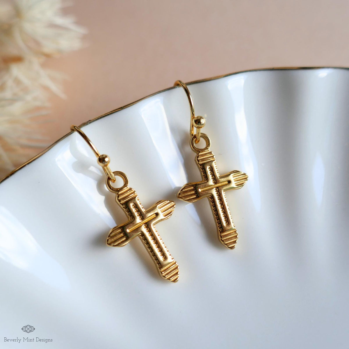 A pair of gold cross-shaped earrings with a scalloped design, displayed on a white surface.