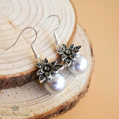 a pair of earrings with pearls on a piece of wood