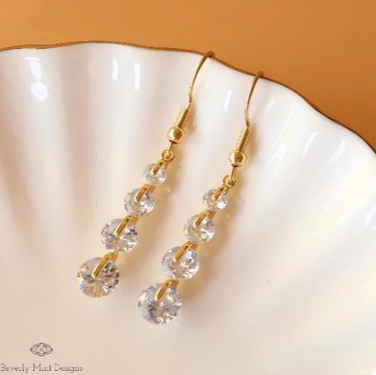 a pair of gold and crystal earrings on a shell