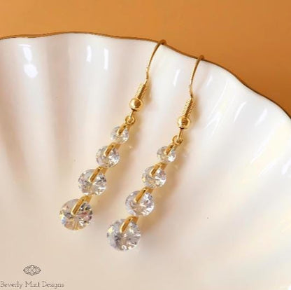 a pair of gold and crystal earrings on a shell