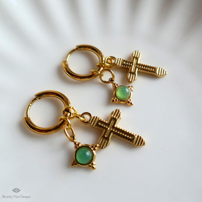a pair of gold earrings with green gemstones, featuring a cross-shaped charm and a round gemstone.