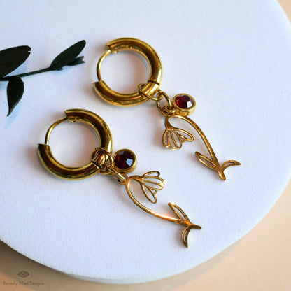 A pair of gold earrings with red gemstones and floral designs, resting on a white surface.