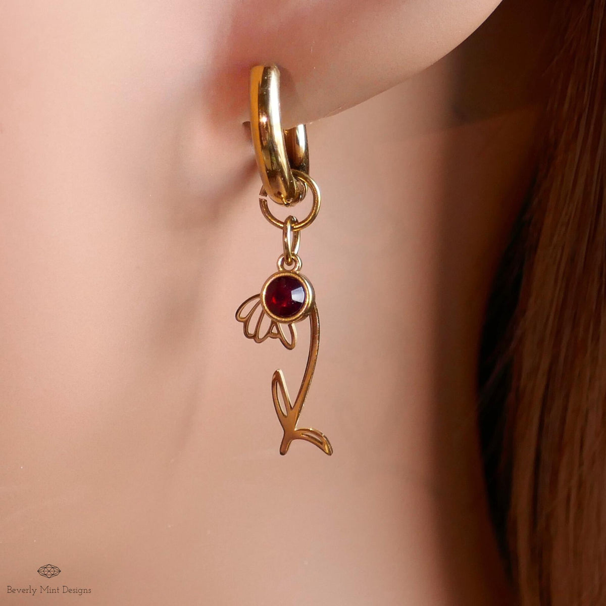 A close-up view of a gold earring with a red gemstone, featuring a delicate flower-like design.