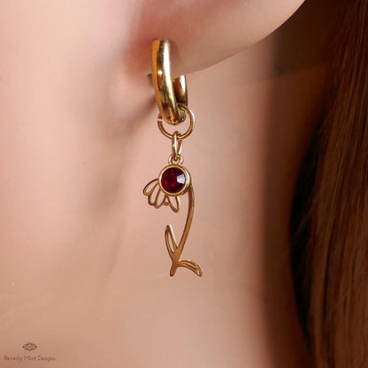 A close-up view of a gold earring with a red gemstone, featuring a delicate flower-like design.