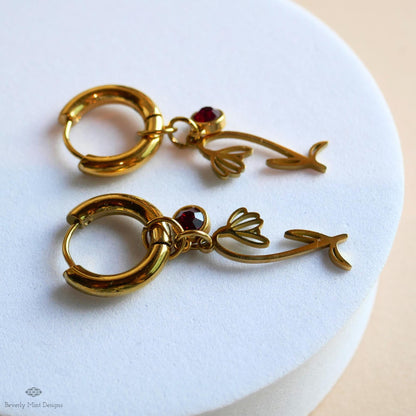 A pair of gold earrings with red gemstones and floral designs, resting on a white surface.