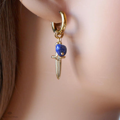 A close-up view of a person's ear wearing a gold earring with a blue gemstone pendant.