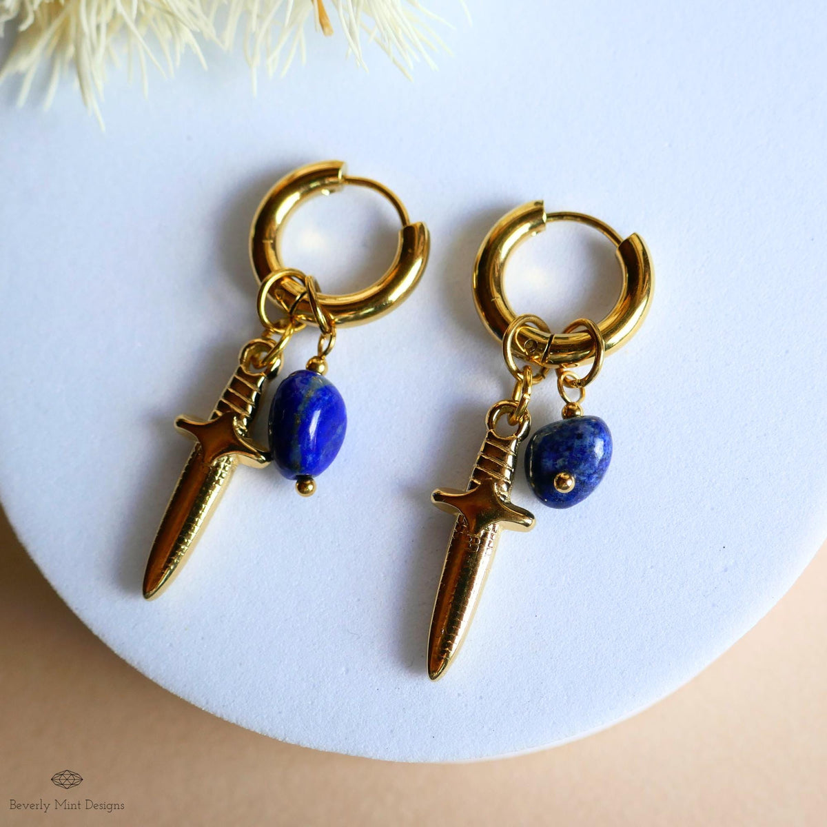 A pair of gold earrings with a blue gemstone and a small blue gemstone dangling from the earrings.