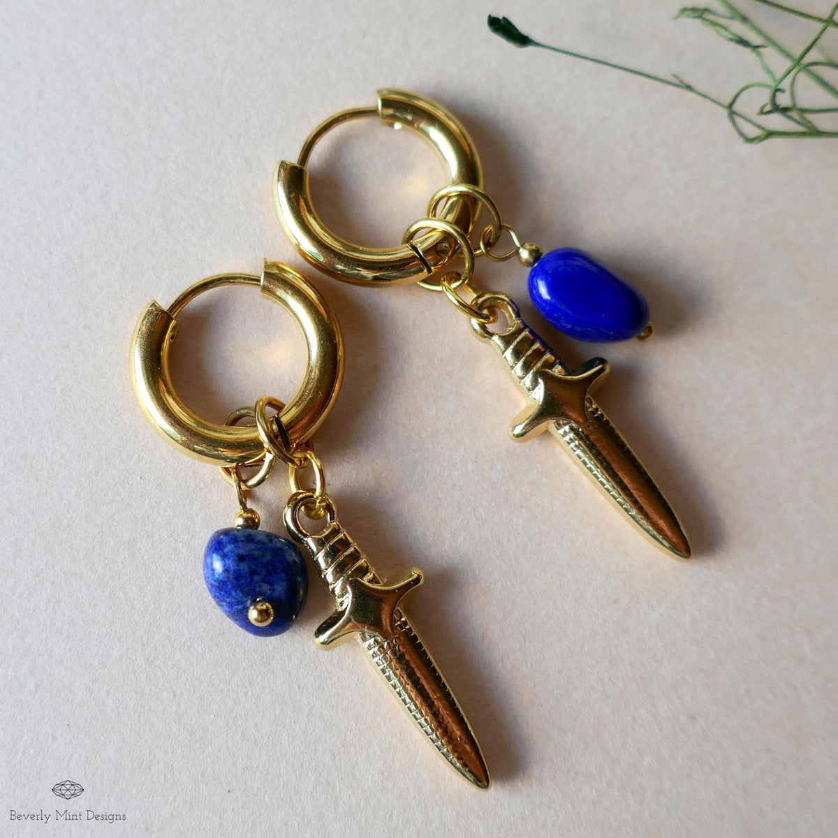 A pair of gold earrings with a blue gemstone and a small charm hanging from them.
