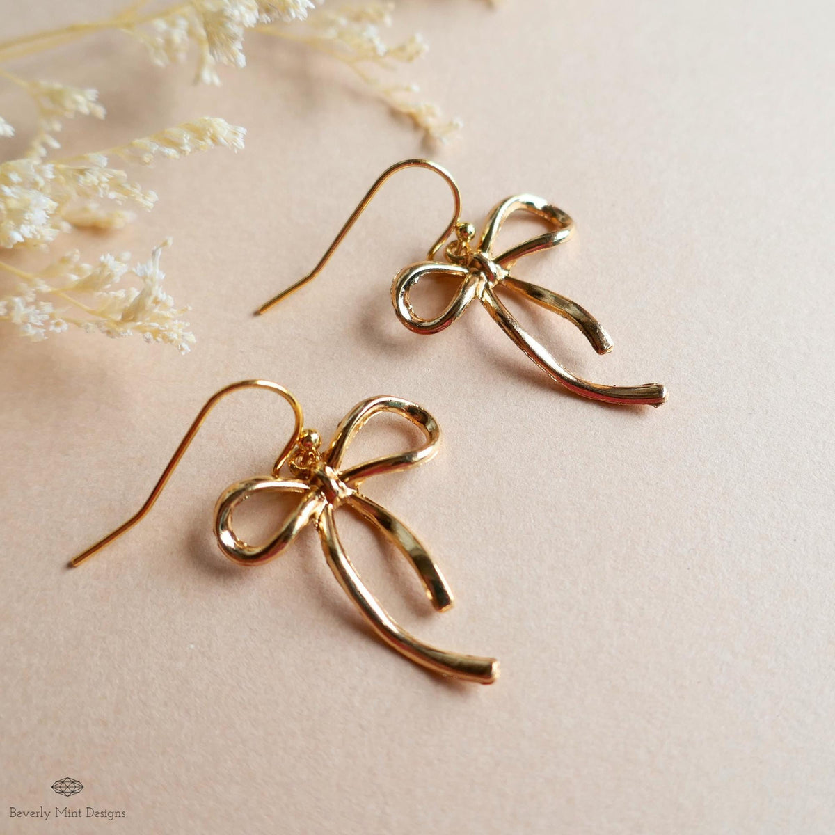 A pair of gold-colored earrings with a bow-shaped design, placed on a light-colored surface.