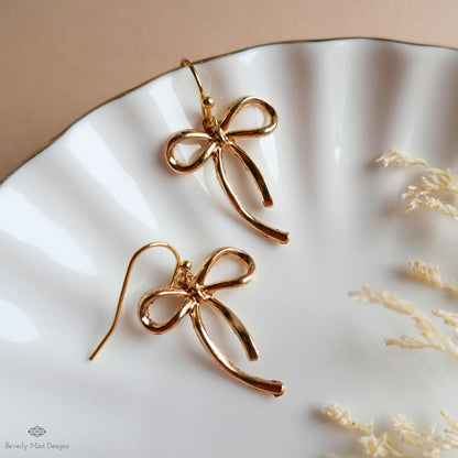 a pair of gold earrings with a bow-shaped design, placed on a white plate.