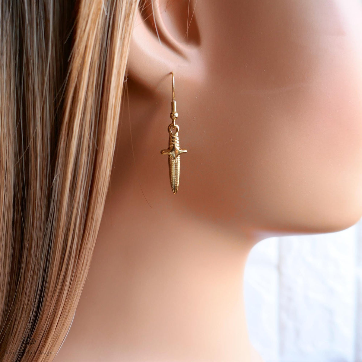 A close-up view of a person's ear wearing a pair of gold earrings with a knife-like design.