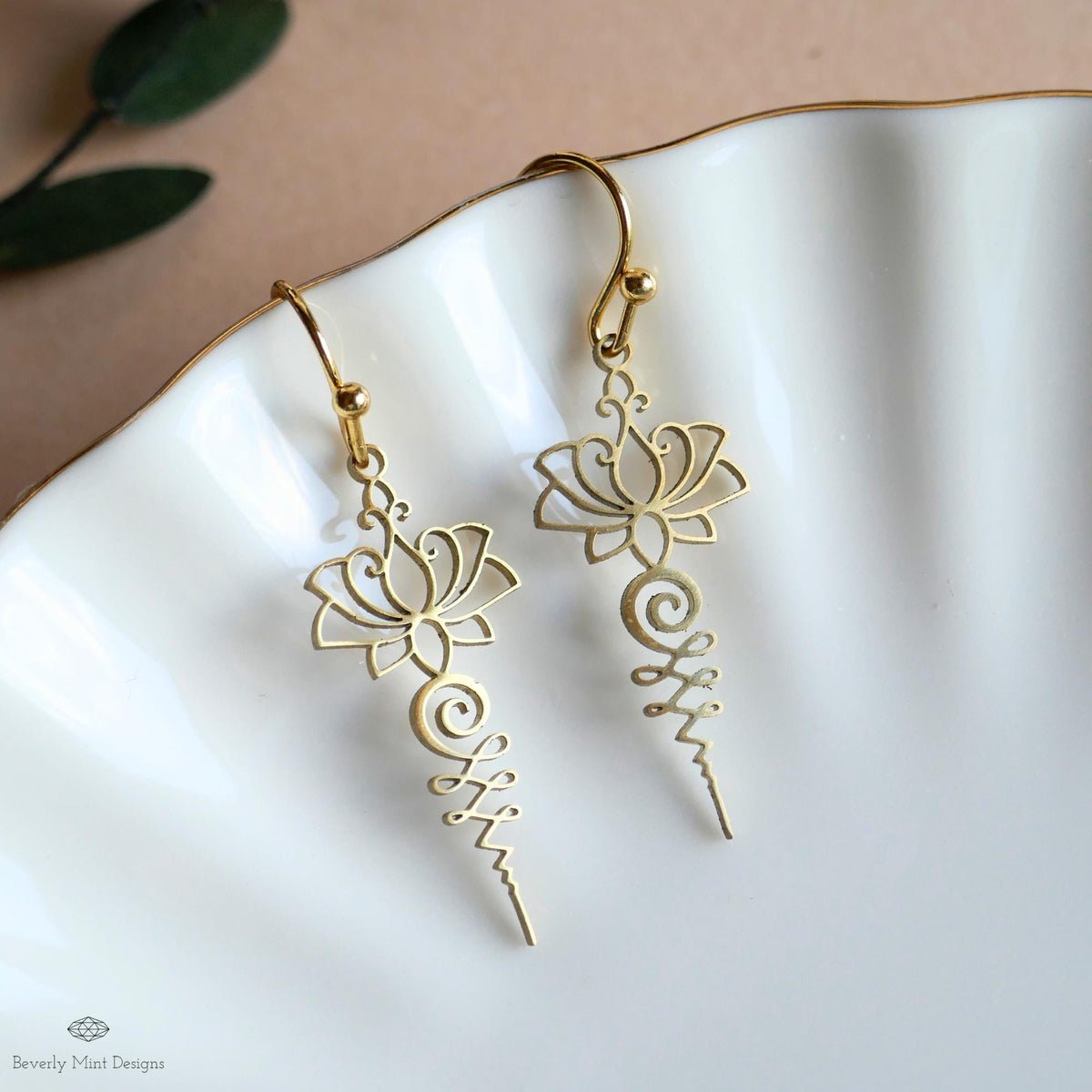 A pair of gold earrings with intricate floral designs, resting on a white plate.