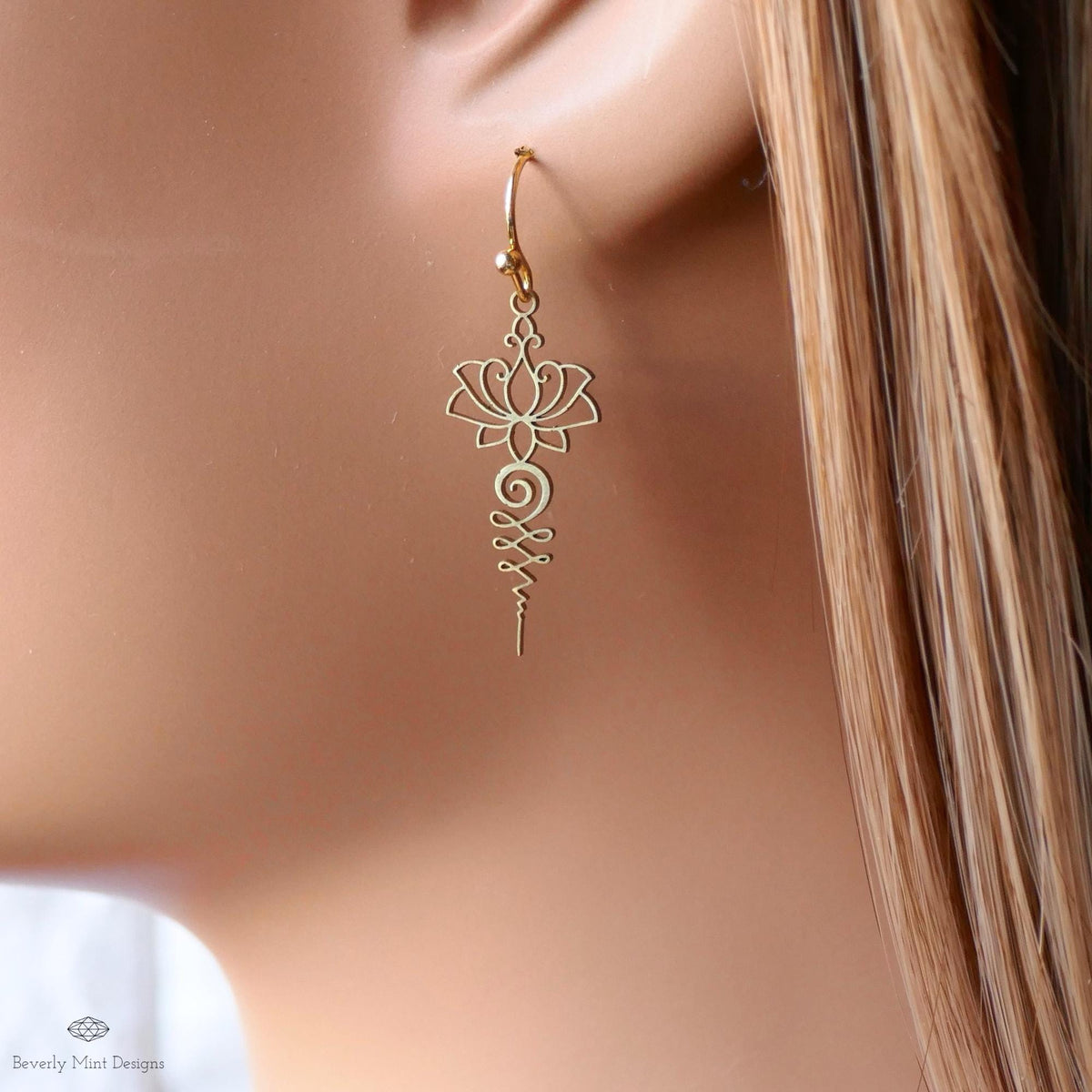 A close-up view of a gold earring with a lotus flower design, hanging from the ear.