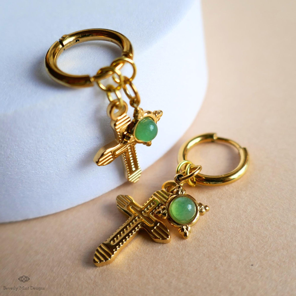two gold cross earrings with green gemstones hanging from them.