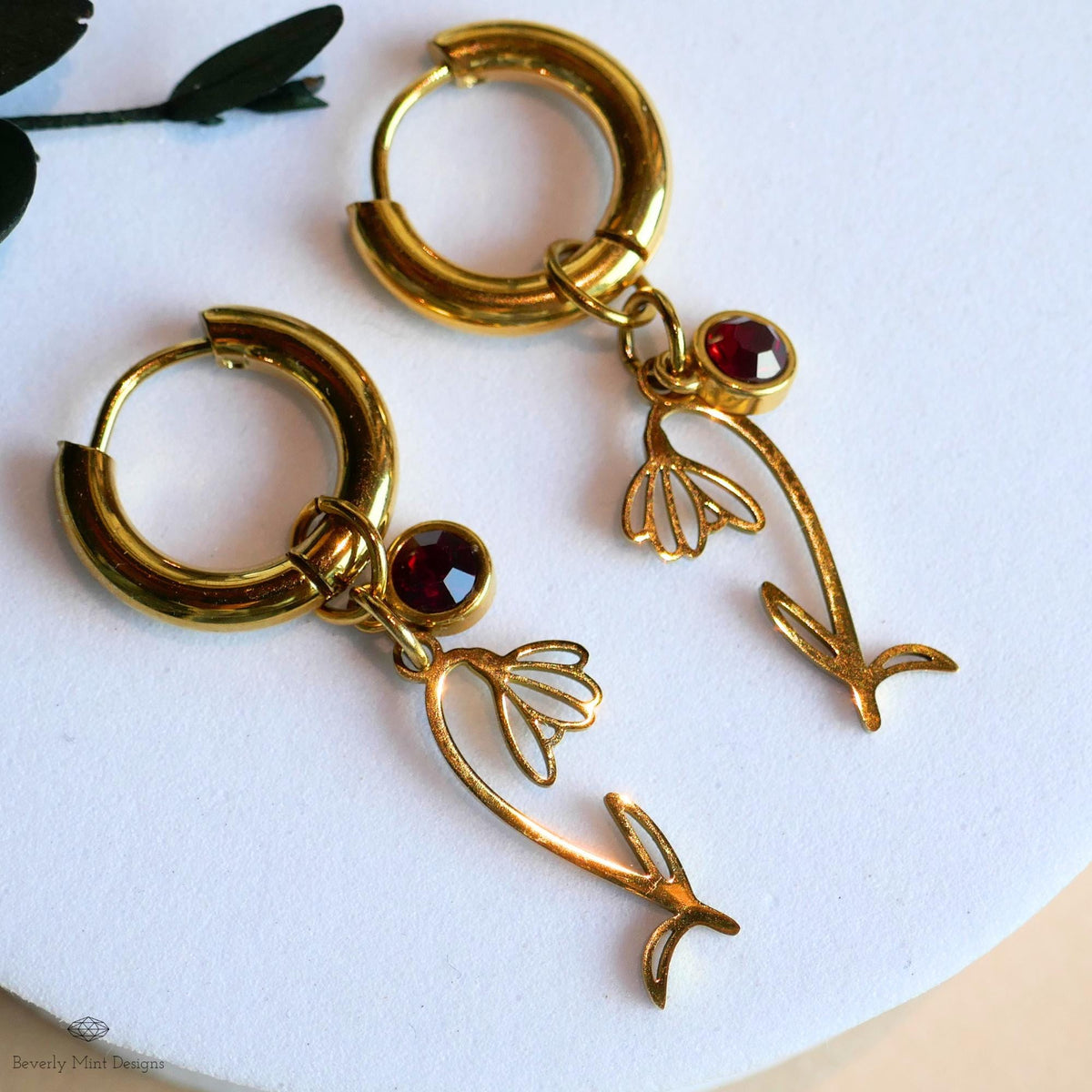 A pair of gold earrings with red gemstones and floral designs, resting on a white surface.