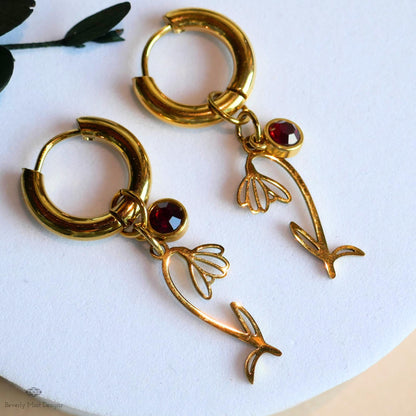A pair of gold earrings with red gemstones and floral designs, resting on a white surface.