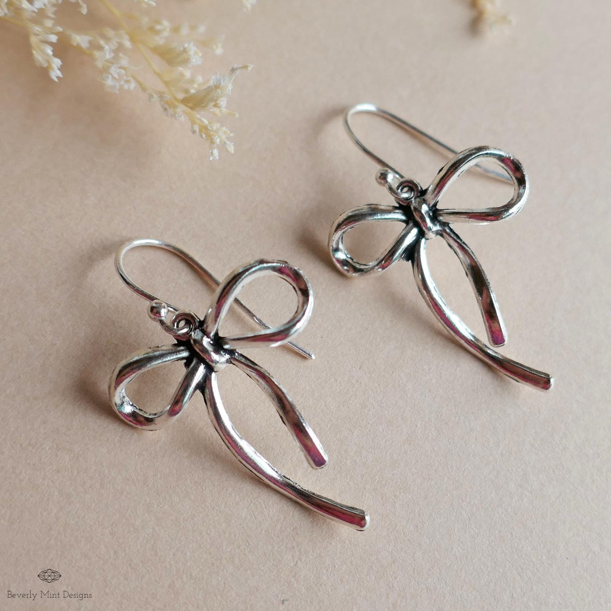 A pair of silver earrings with a bow-shaped design, placed on a beige background.