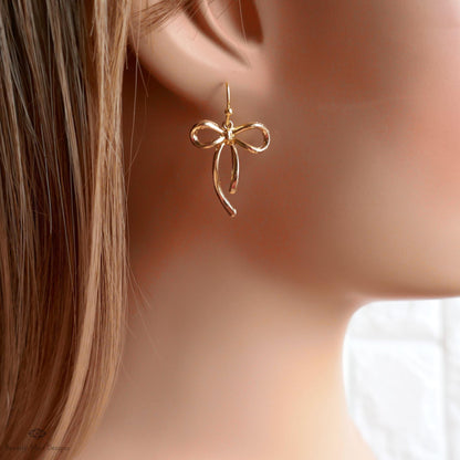 A close-up view of a person's ear wearing a pair of gold-colored earrings with a bow-shaped design.