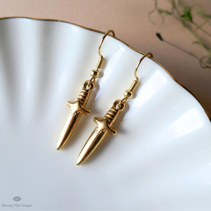 A pair of gold-colored earrings with a pointed design, resting on a white plate.