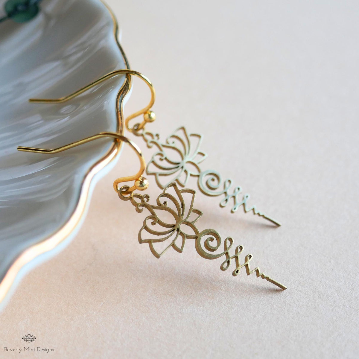 A pair of gold earrings with intricate floral designs, resting on a white surface.
