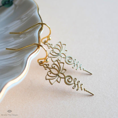 A pair of gold earrings with intricate floral designs, resting on a white surface.
