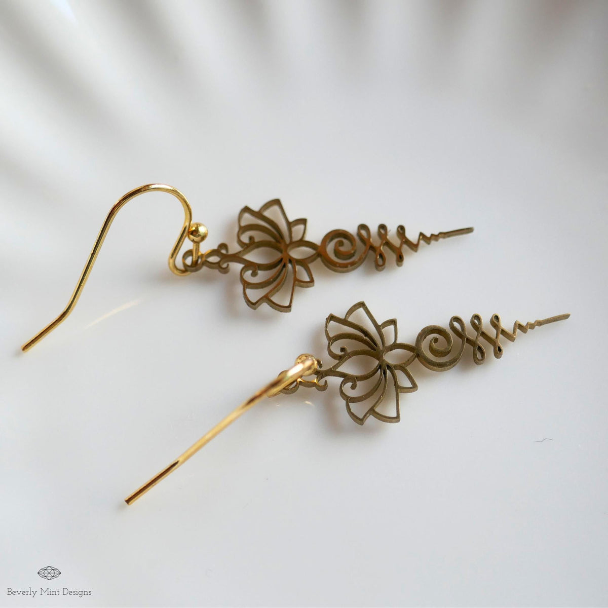 A pair of gold earrings with intricate floral designs, resting on a white surface.