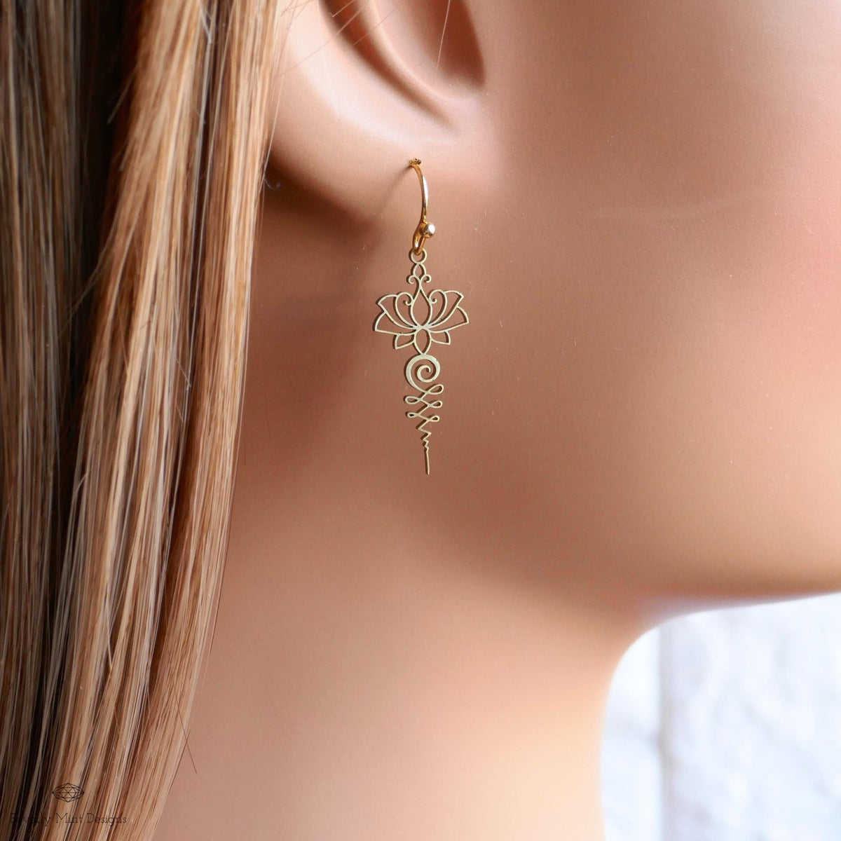 A close-up view of a person's ear wearing a pair of gold earrings with a delicate floral design.